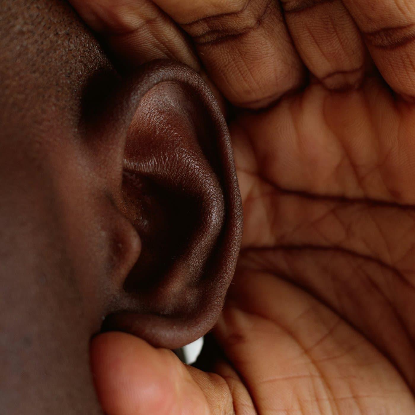 Close-up of someone cupping a hand near their ear to hear better