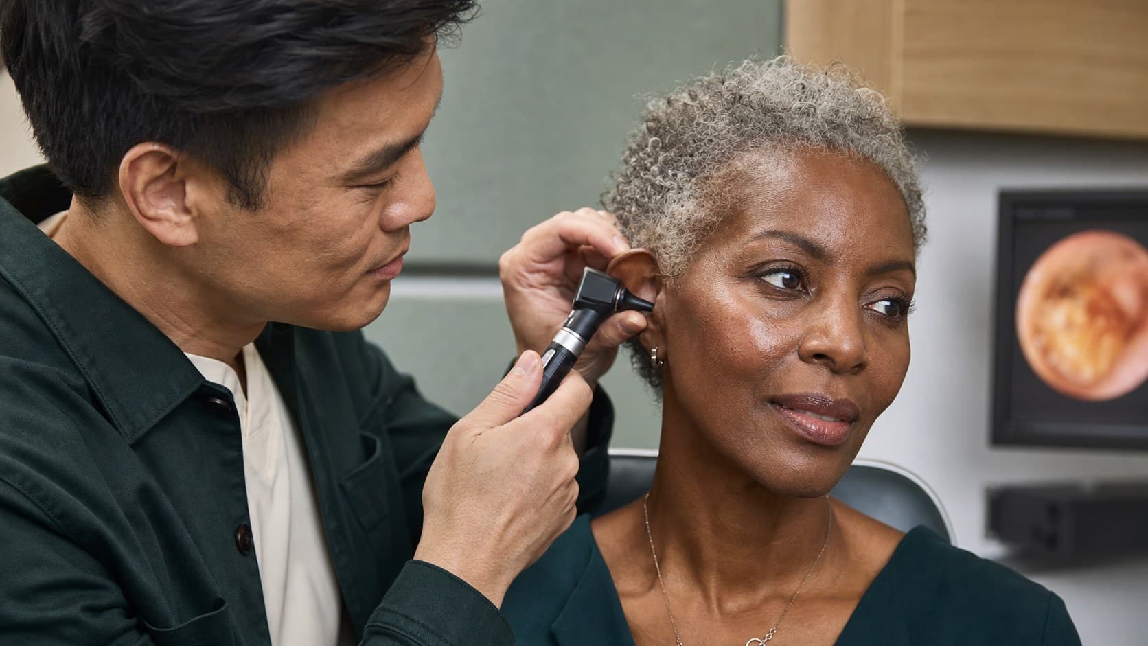 An audiologist examining a patient's ear with an otoscope during a follow-up check